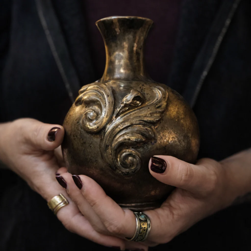 Handmade gothic stoneware vase with metallic bronze glaze and intricate relief carvings, held by a ceramicist.