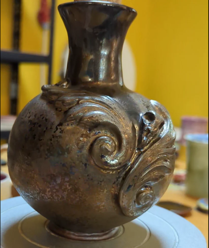 Handmade gothic stoneware vase with metallic bronze glaze and intricate relief carvings, held by a ceramicist.
